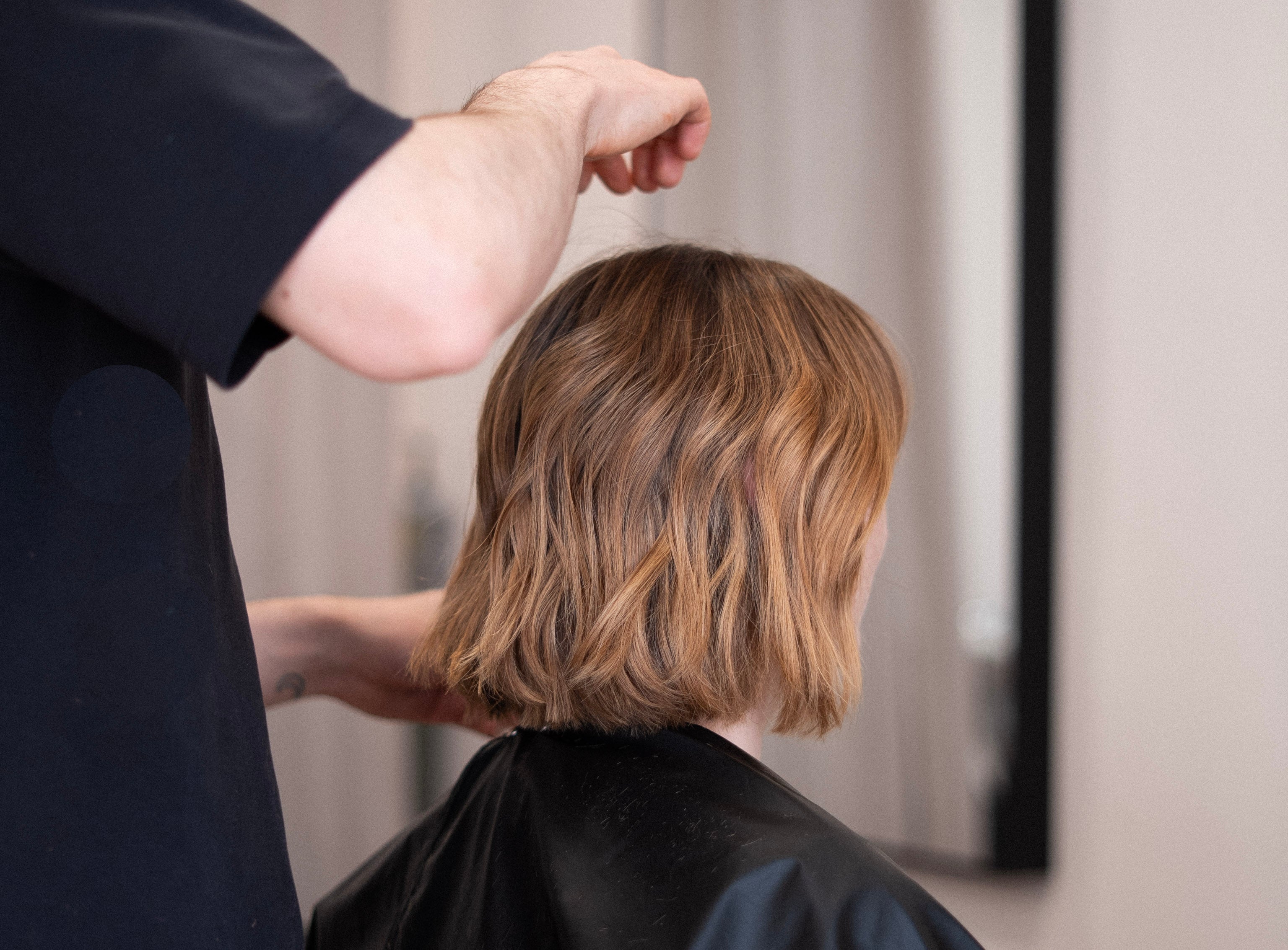Person getting a haircut with a stylist adjusting hair in a salon setting.